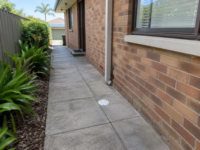 Brick house side path with a round drain cover set in paved ground in Collaroy