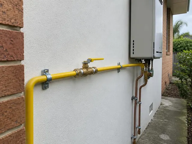 Yellow gas pipe and shutoff valve beside an exterior wall-mounted heater in a brick home in Mona Vale